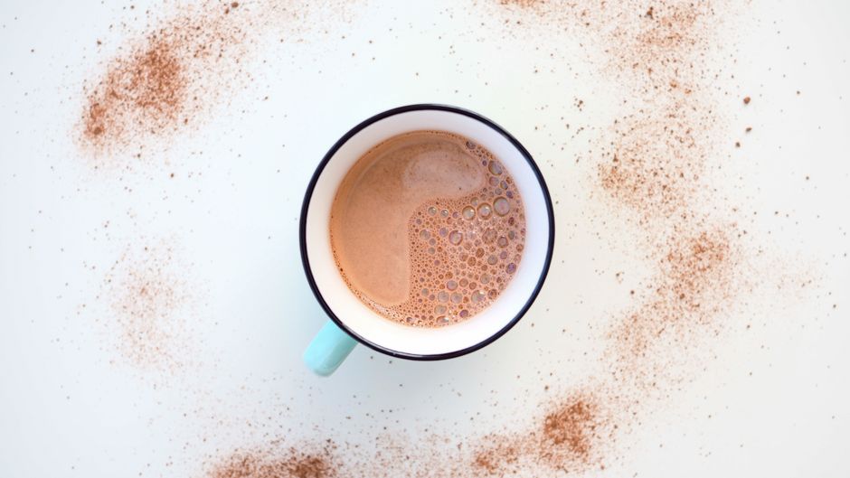 Top view of a steaming hot chocolate mug with cocoa sprinkles on a white surface.